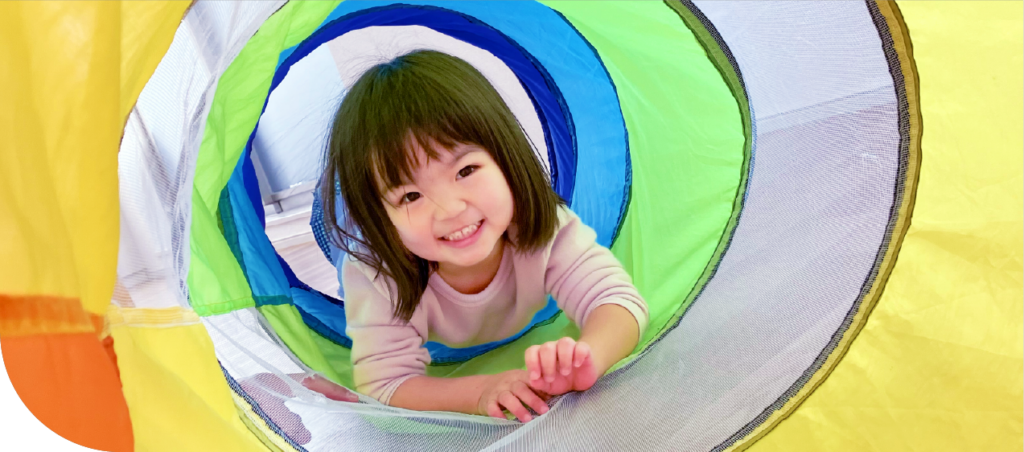 園児が虹色のカラフルなトンネル遊具で楽しく遊んでいる姿