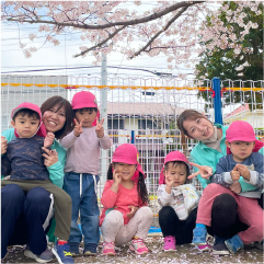 公園の桜の前での記念写真。先生と園児が写っている。