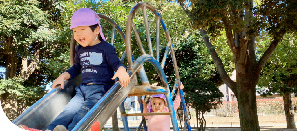 年齢の違う園児が公園の滑り台で一緒に遊んでいる。