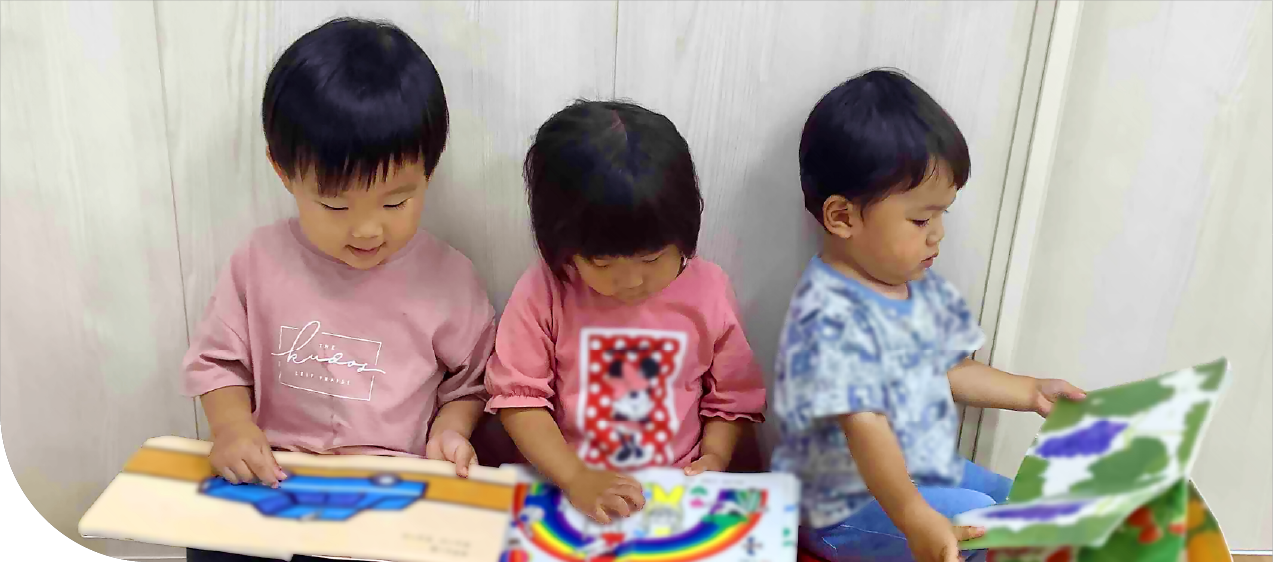 3人の園児が室内で集中して絵本を読んでいる。
